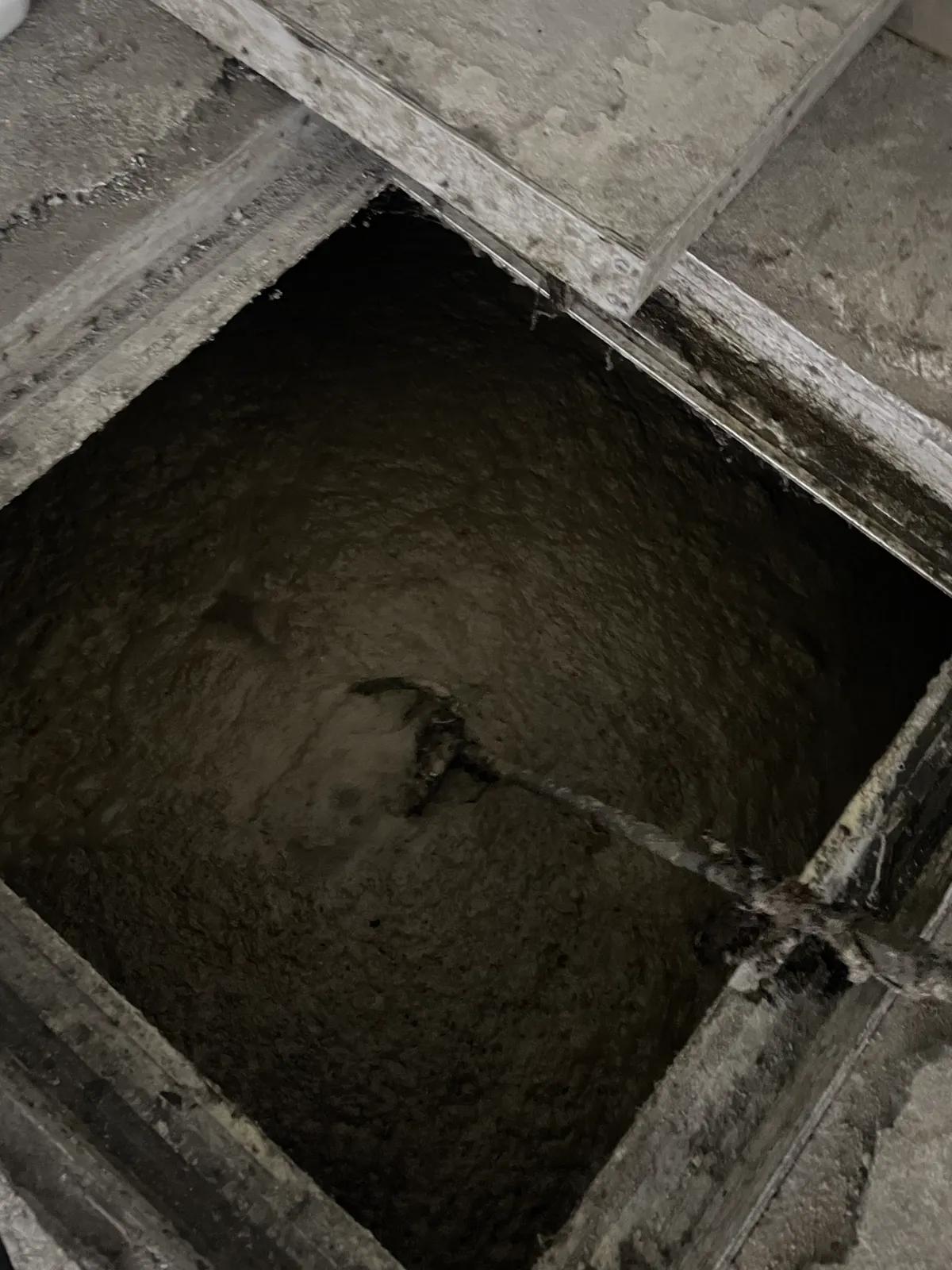 Caixa de gordura de concreto com duas câmaras e tampas removidas, tomada por gordura acumulada