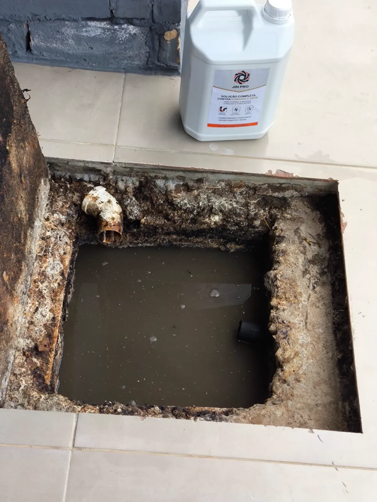 Caixa de gordura limpa depois da aplicação do JIN PRO, com a água à vista e o galão apoiado na borda