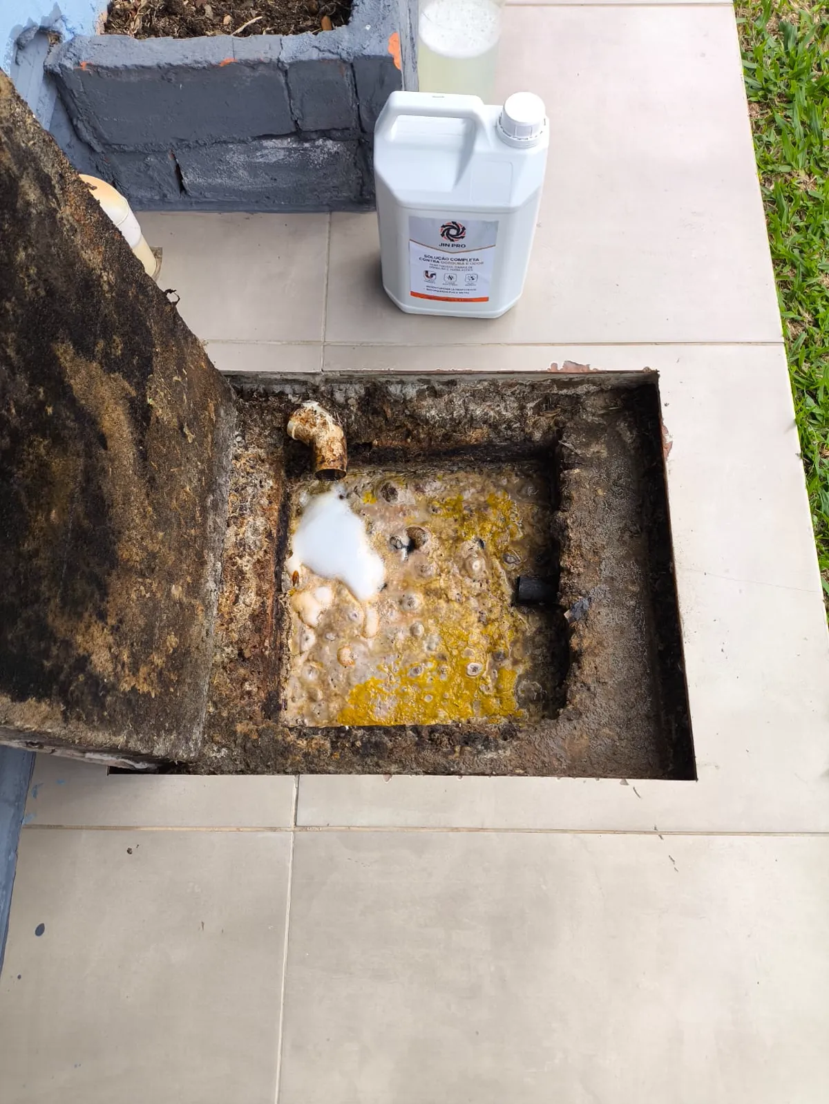 Caixa de gordura aberta com o produto começando a dissolver a camada de gordura e o galão de JIN PRO ao lado